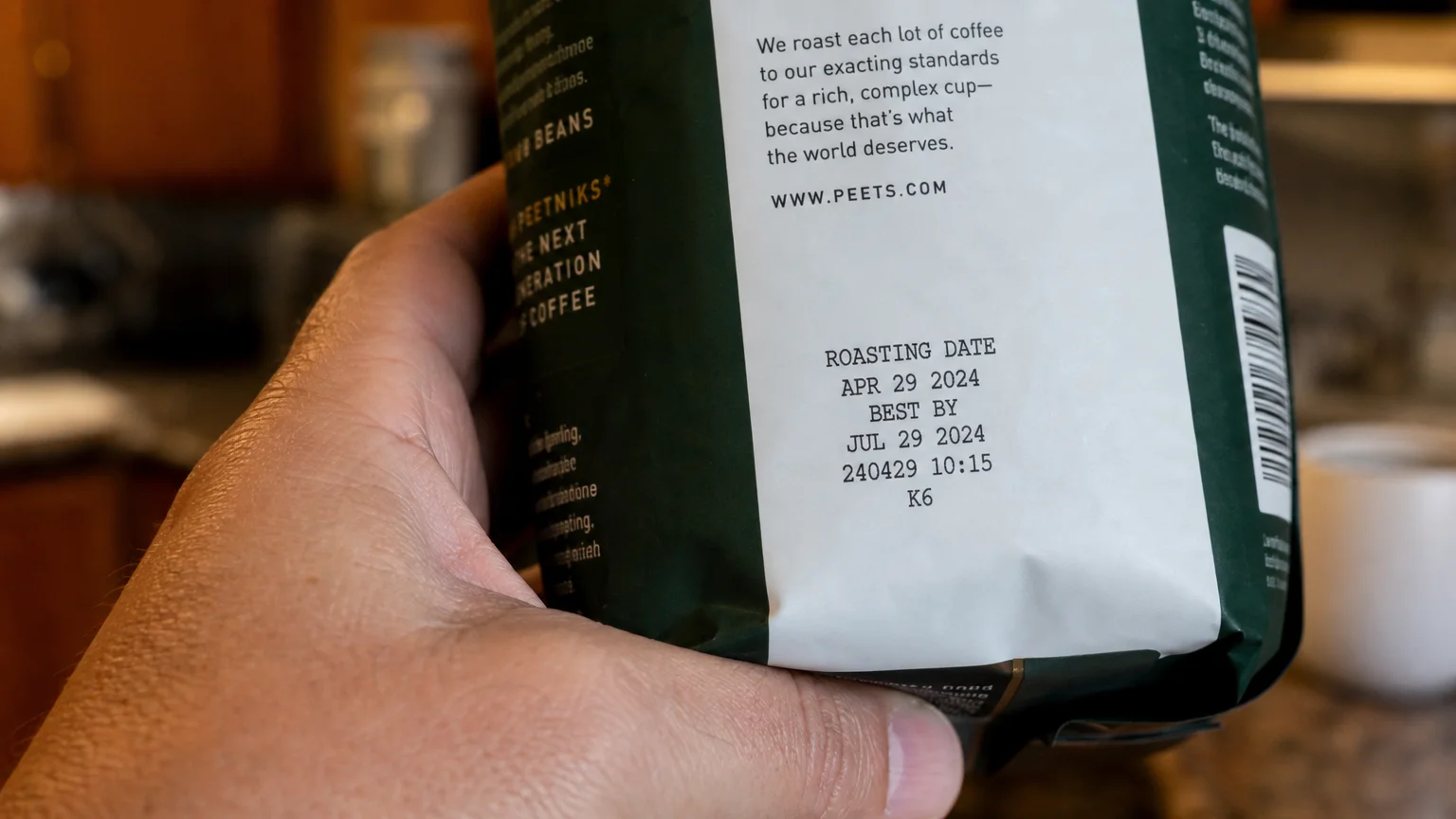 A close-up of a hand pointing to the roasting date printed on a bag of Peet's coffee.