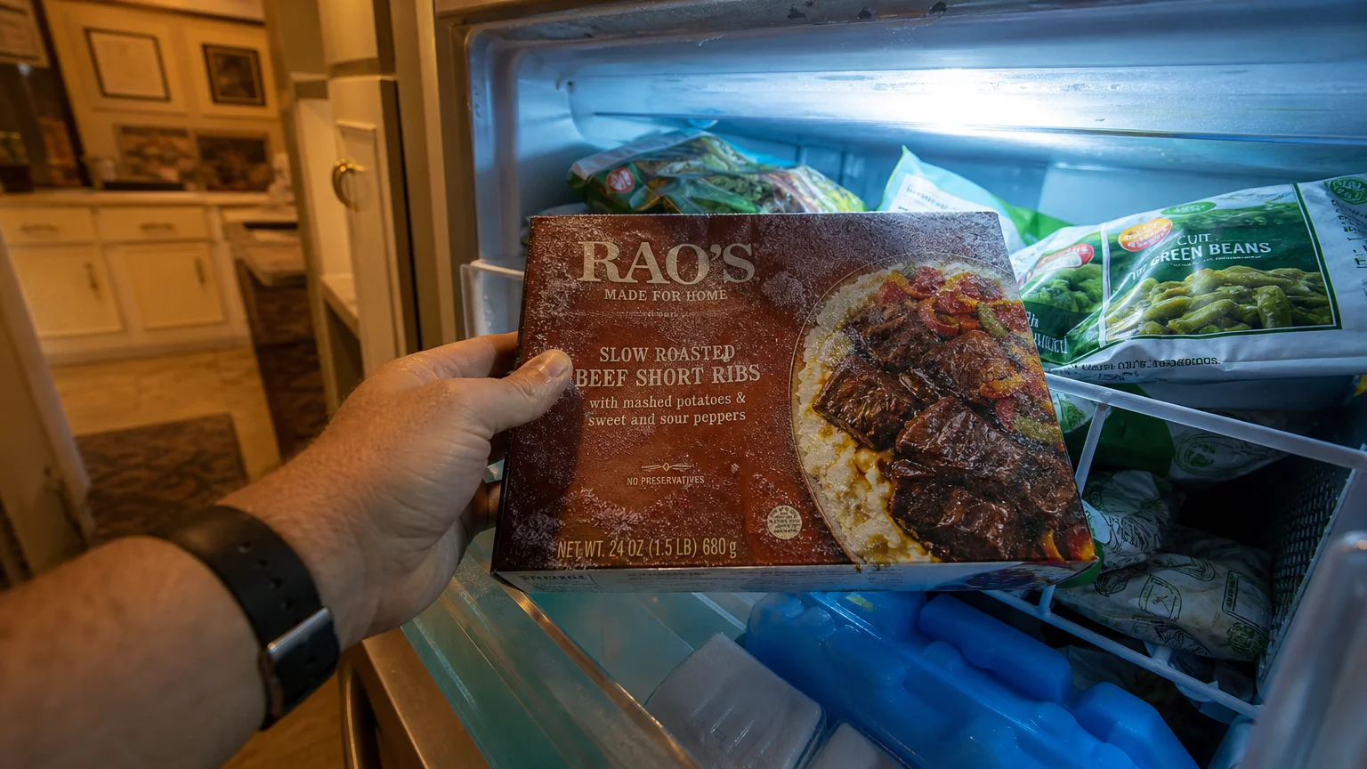 A first-person view of a hand reaching into a home freezer to select a premium frozen meal box.