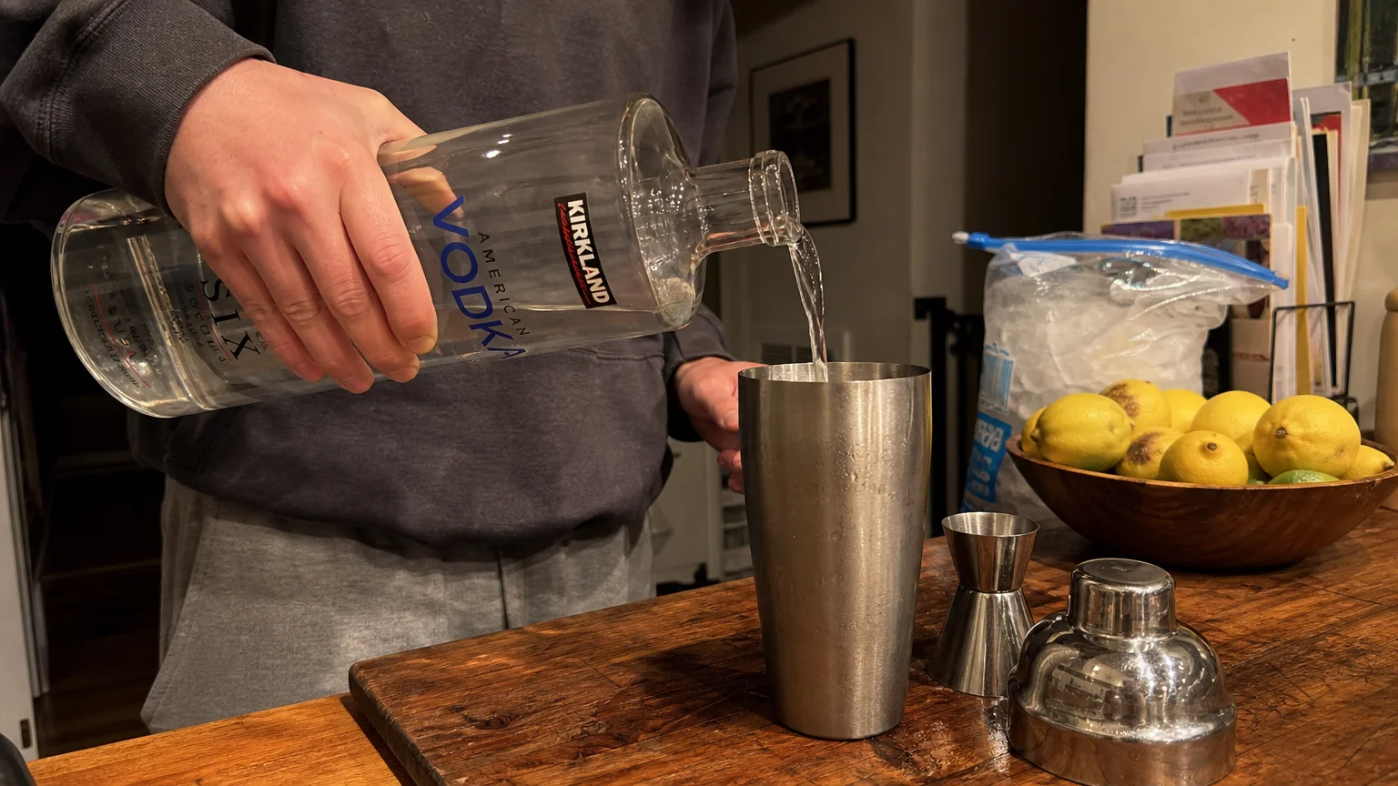 A person pouring Kirkland vodka into a shaker in a cozy, real-life kitchen setting.