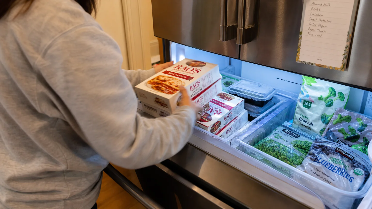 A person stocking their home freezer with frozen lasagna boxes, representing a strategic supermarket stock-up.